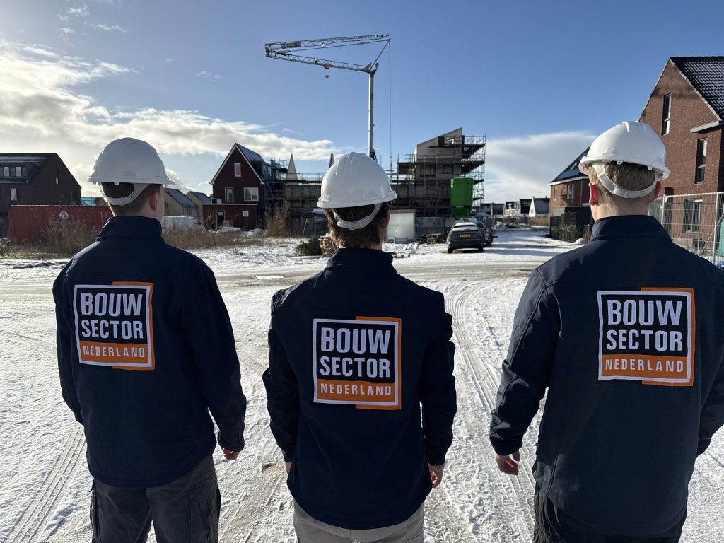 Drie vakmensen van Bouwsector Nederland met witte helm op een besneeuwde straat met nieuwbouw